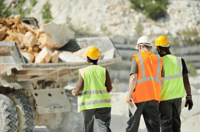 constructions workers walk on a road where a construction truck is parked