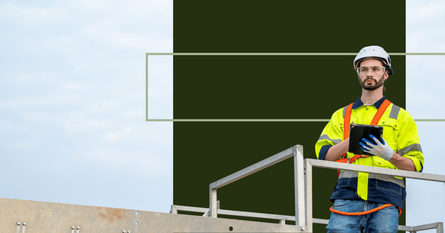 a construction worker holds a tablet while looking into the distance