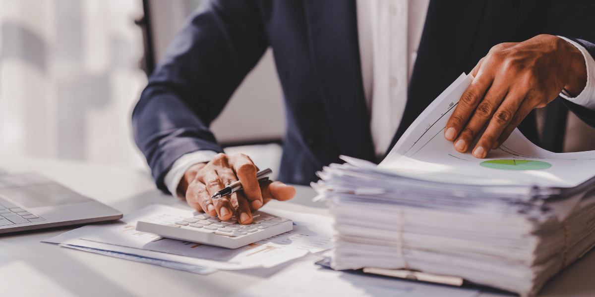 man looking at a stack of paperwork and calculator auditing payroll