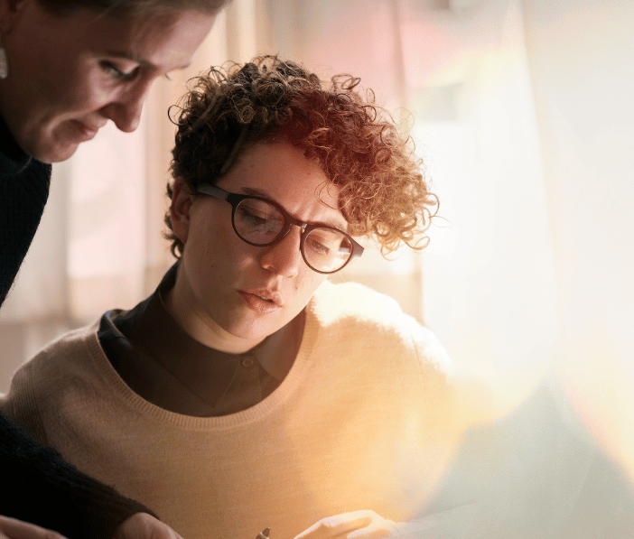 decorative: coworkers focus on laptop while sun shines in through a window decorative: coworkers focus on laptop while sun shines in through a window