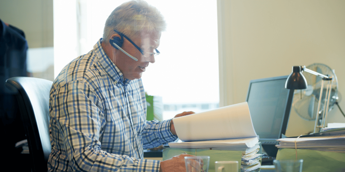 employee focused on a stack of paperwork while on the phone employee focused on a stack of paperwork while on the phone