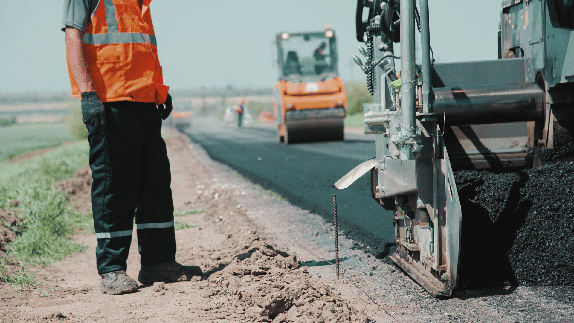 worker stands by equipment on road construction site.
