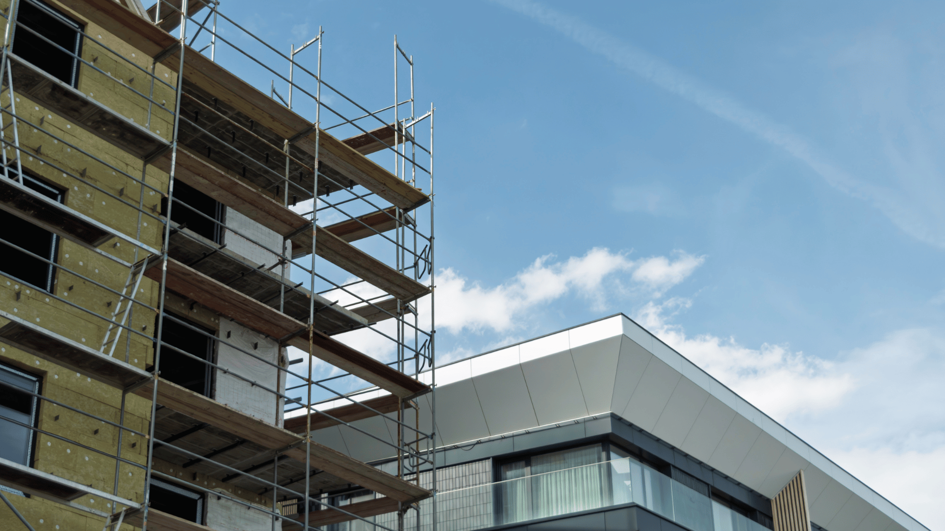 Scaffolding covers building under insulation installation, next to finished modern facade
